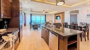 A modern kitchen with granite countertops, a dishwasher, and a dining area with wooden chairs and a large island. - Dolphin Paradise  (South Padre Island)