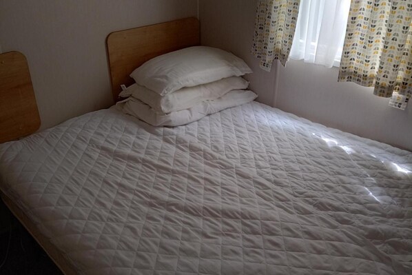 A bed with a wooden headboard, white bedding, and a window with patterned curtains.