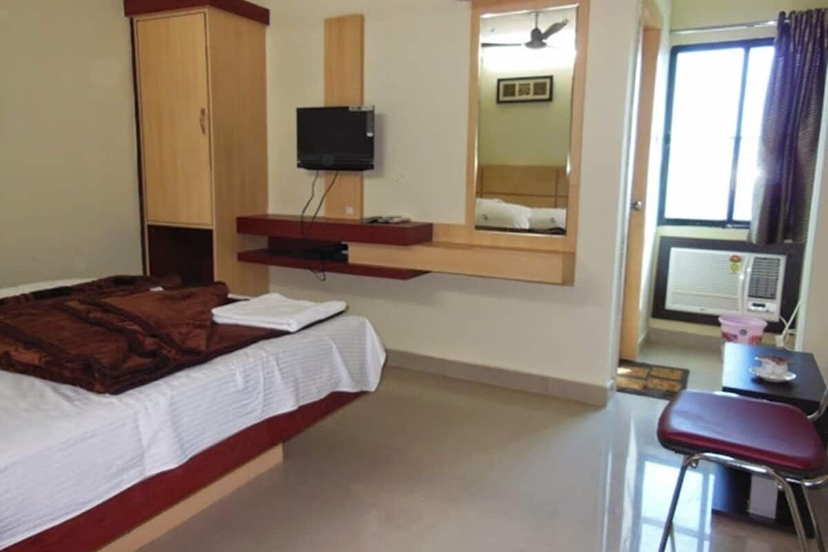 Una habitación de hotel con cama, escritorio, televisión y ventana con cortinas.