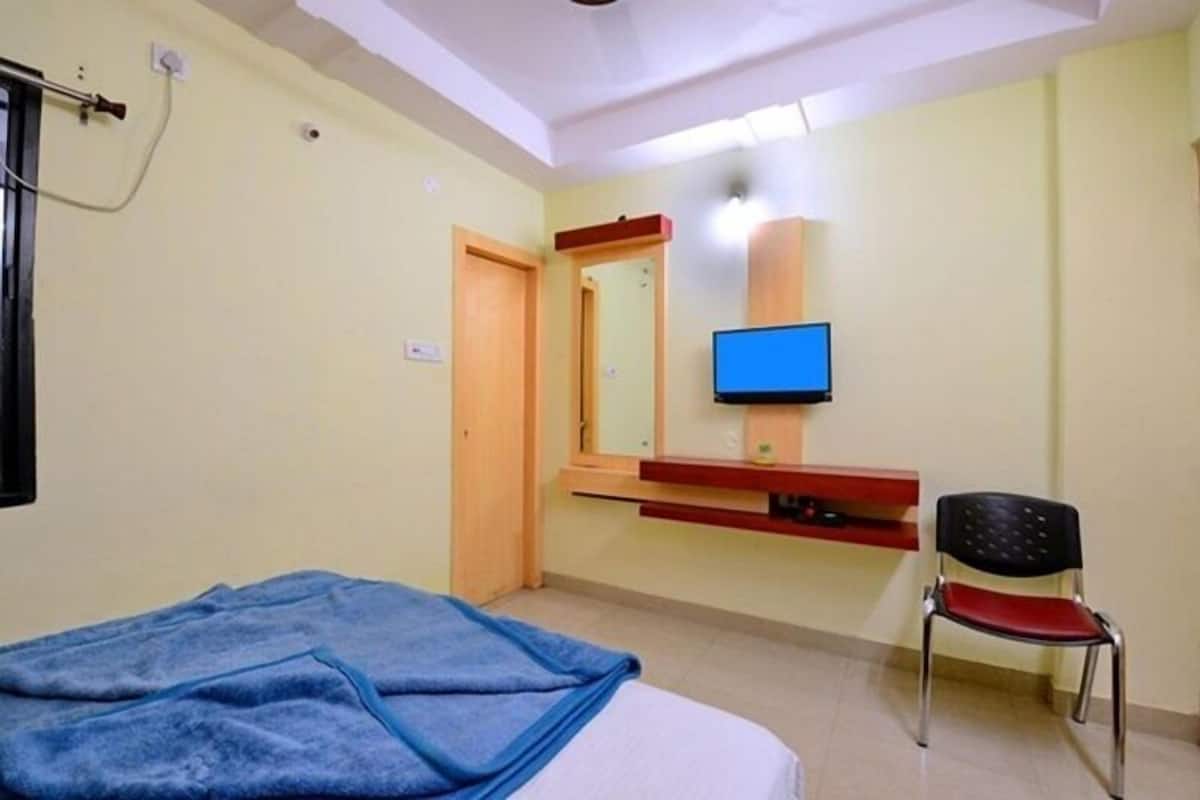 Una habitación con cama, silla, televisión y espejo.