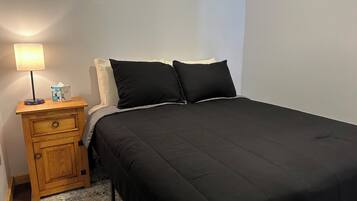 Ein Bett mit schwarzer Bettwäsche, ein Nachttisch aus Holz mit einer Lampe und einer Taschentuchbox.