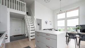 Une cuisine moderne avec un îlot central blanc, des armoires grises et un escalier menant à un niveau supérieur.