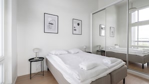 Une chambre à coucher moderne avec un grand lit, une table de chevet avec une lampe et des œuvres d’art encadrées accrochées au mur.