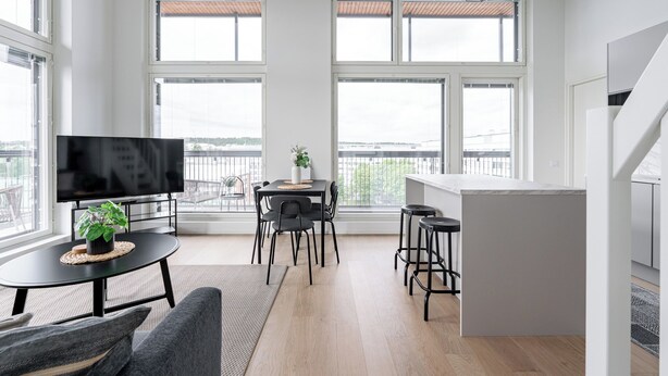 Un salon moderne doté d’un téléviseur à écran plat, d’une table à manger avec des chaises et d’un coin cuisine avec des tabourets.