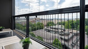 Un balcon offrant une vue sur le paysage urbain, notamment sur un grand bâtiment doté d’une structure de toit originale.