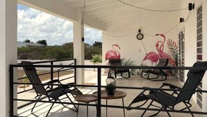 A covered outdoor seating area with chairs and a table, a clock, and a wall mural of flamingos.