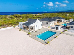 Una propiedad frente a la playa con varios edificios blancos, una piscina y vista al océano.
