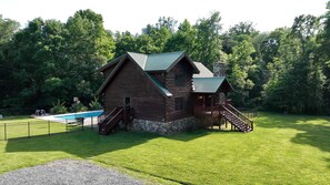 Eine Blockhütte mit Schwimmbad, umgeben von einem eingezäunten Garten und üppiger Vegetation.