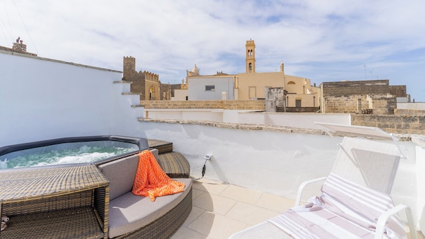 Eine Dachterrasse mit Whirlpool, Liegestühlen und Blick auf historische Gebäude.