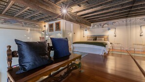A room with a wooden ceiling, a bed with white bedding, and a table with two blue pillows. - Casa Savoia by Wonderful Italy (Turin)