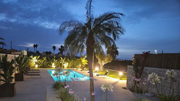 A swimming pool surrounded by plants and palm trees, with lounge chairs and a stone wall. - Villa Merilusi by Ortigiaapartments (Syracuse)