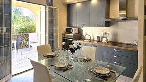 A modern kitchen with a glass dining table set for six, a microwave, oven, and a coffee maker. - Villa Merilusi by Ortigiaapartments (Syracuse)