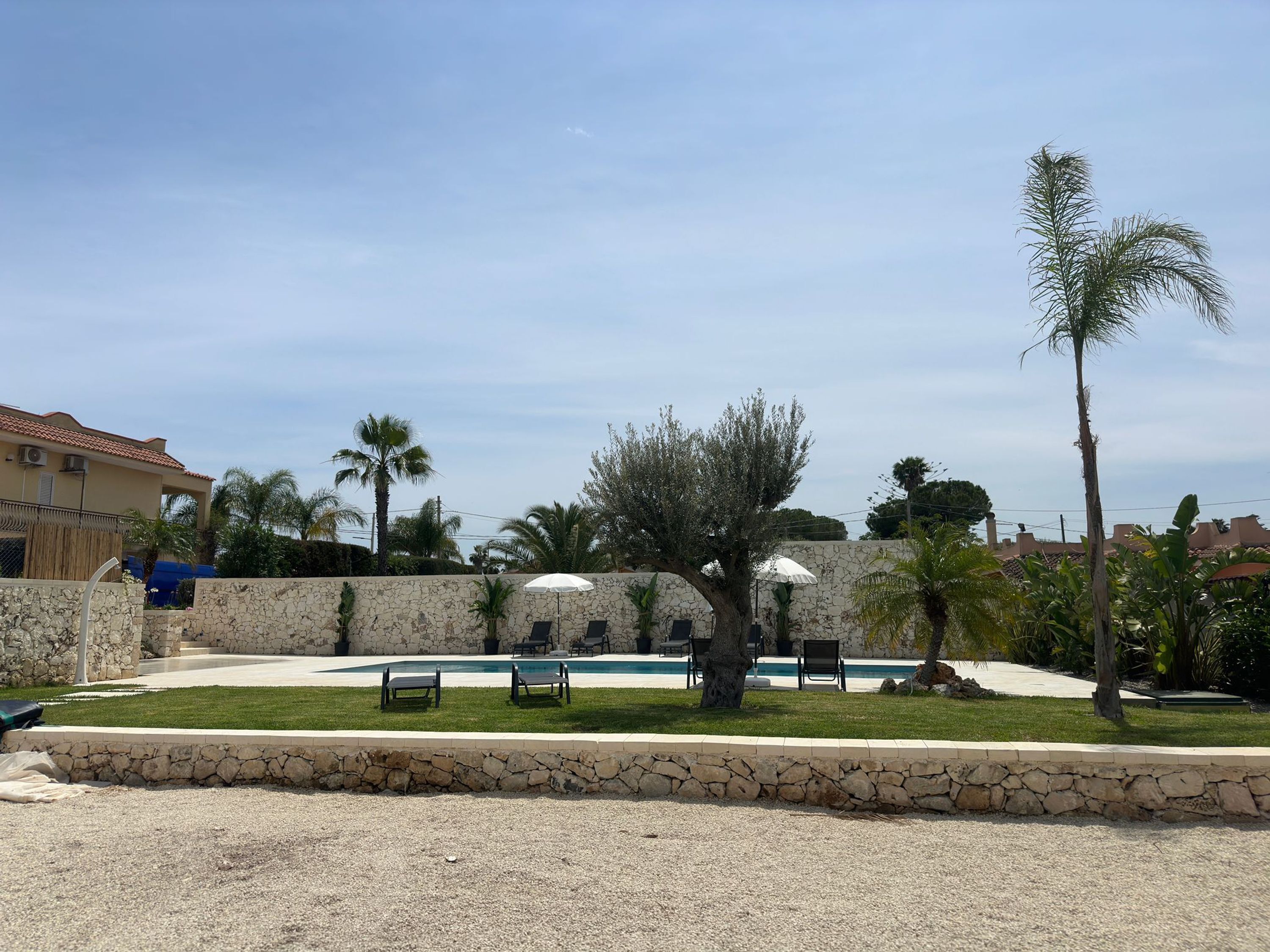 A pool area with lounge chairs, a stone wall, and palm trees.