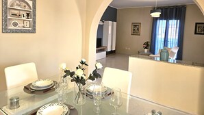 A dining area with a glass table set for four, surrounded by white chairs. There is a framed picture on the wall above the table. - Villa Merilusi by Ortigiaapartments (Syracuse)