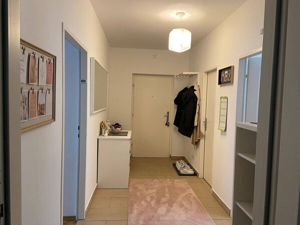 Um corredor com uma porta branca, um cabideiro, uma pequena mesa com um cesto e um tapete rosa.