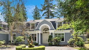 A two-story house with a grey exterior, a central entrance with an arched doorway, and a number '8115' on the front.