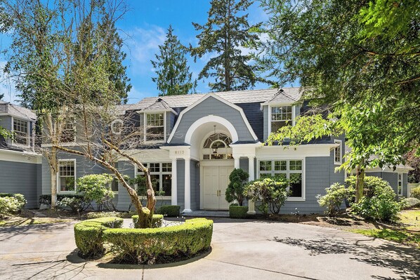 A two-story house with a grey exterior, a central entrance with an arched doorway, and a number '8115' on the front.