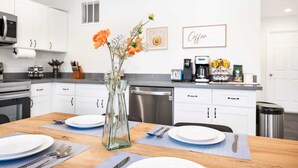 A modern kitchen with white cabinets, a dining table set with plates, cutlery, and a vase with flowers.