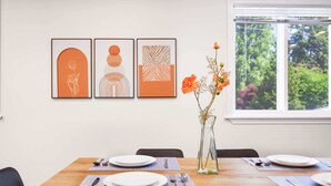 A dining table set with plates, cutlery, and a vase with flowers. Three framed artworks are displayed on the wall above the table.