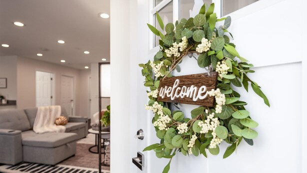 A white door with a 'welcome' sign and a wreath of green leaves and white berries.