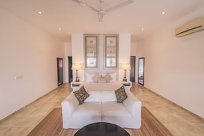A spacious living area with a white sofa, two side tables with lamps, a ceiling fan, and a large window with decorative panels. - Villa Thuya (Balapitiya)