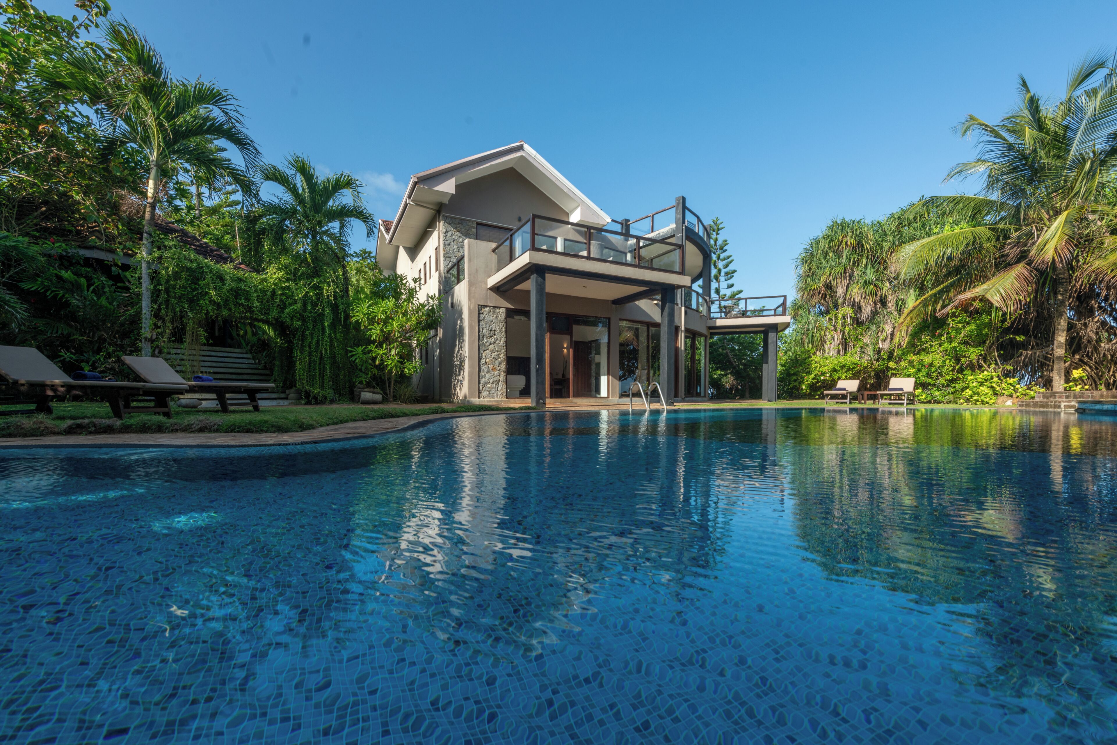 A modern house with a pool, surrounded by palm trees and a clear sky.