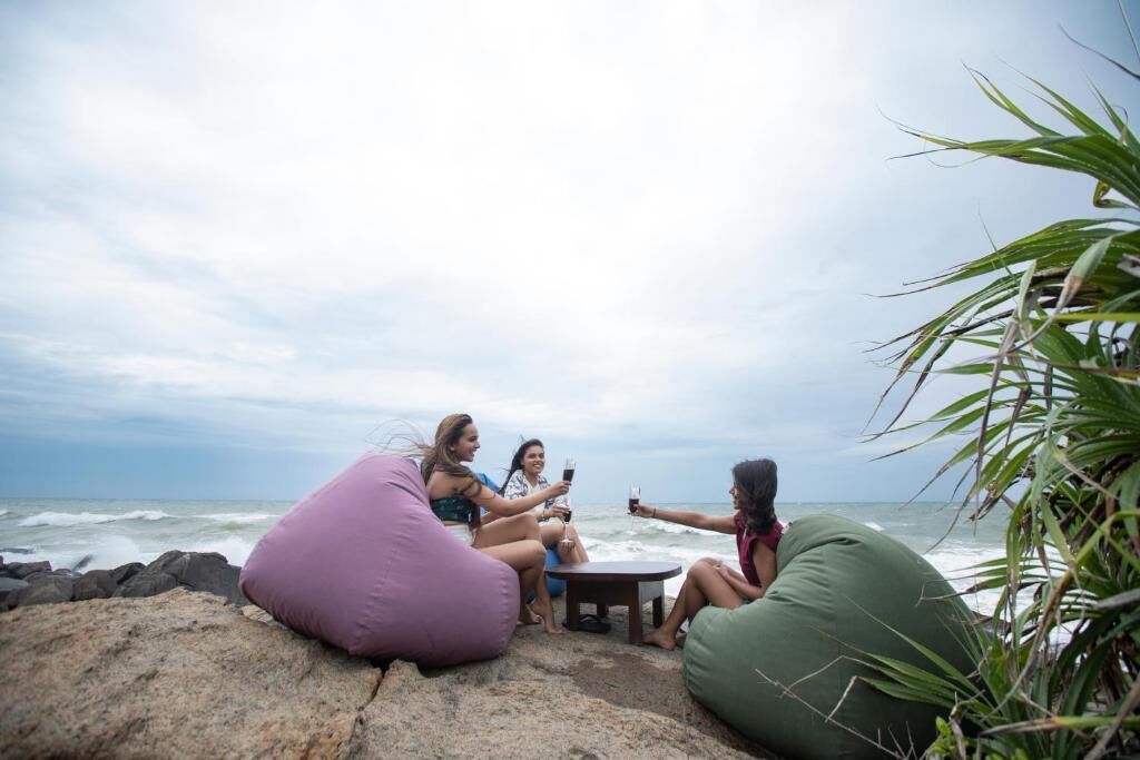 Three people sitting on bean bags by the ocean, with a view of the sea and cloudy sky.