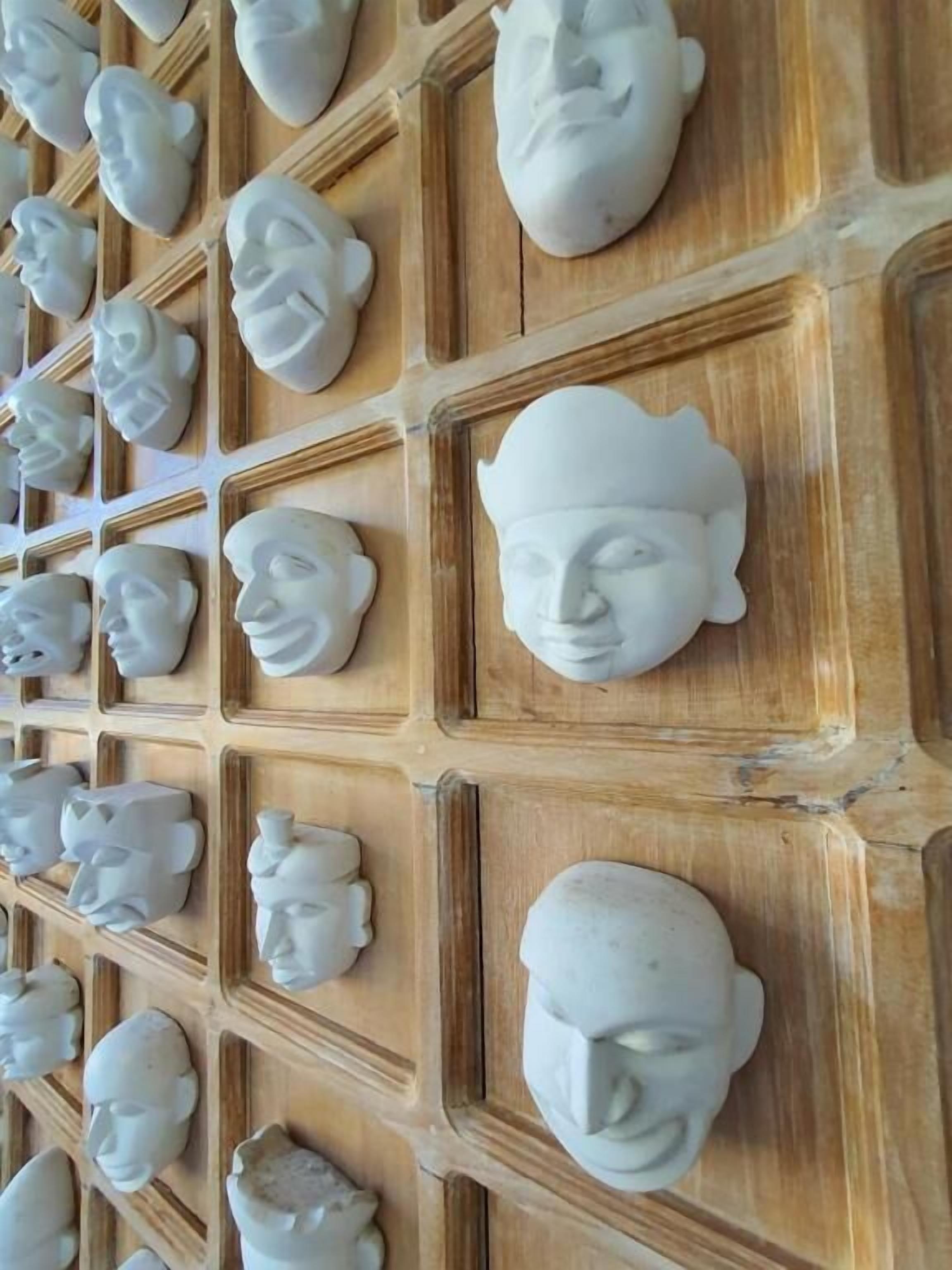 A wall with multiple white, sculptural faces arranged in a grid pattern.