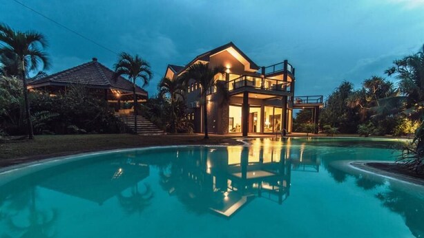 Ein modernes Haus mit Swimmingpool, umgeben von tropischer Vegetation.