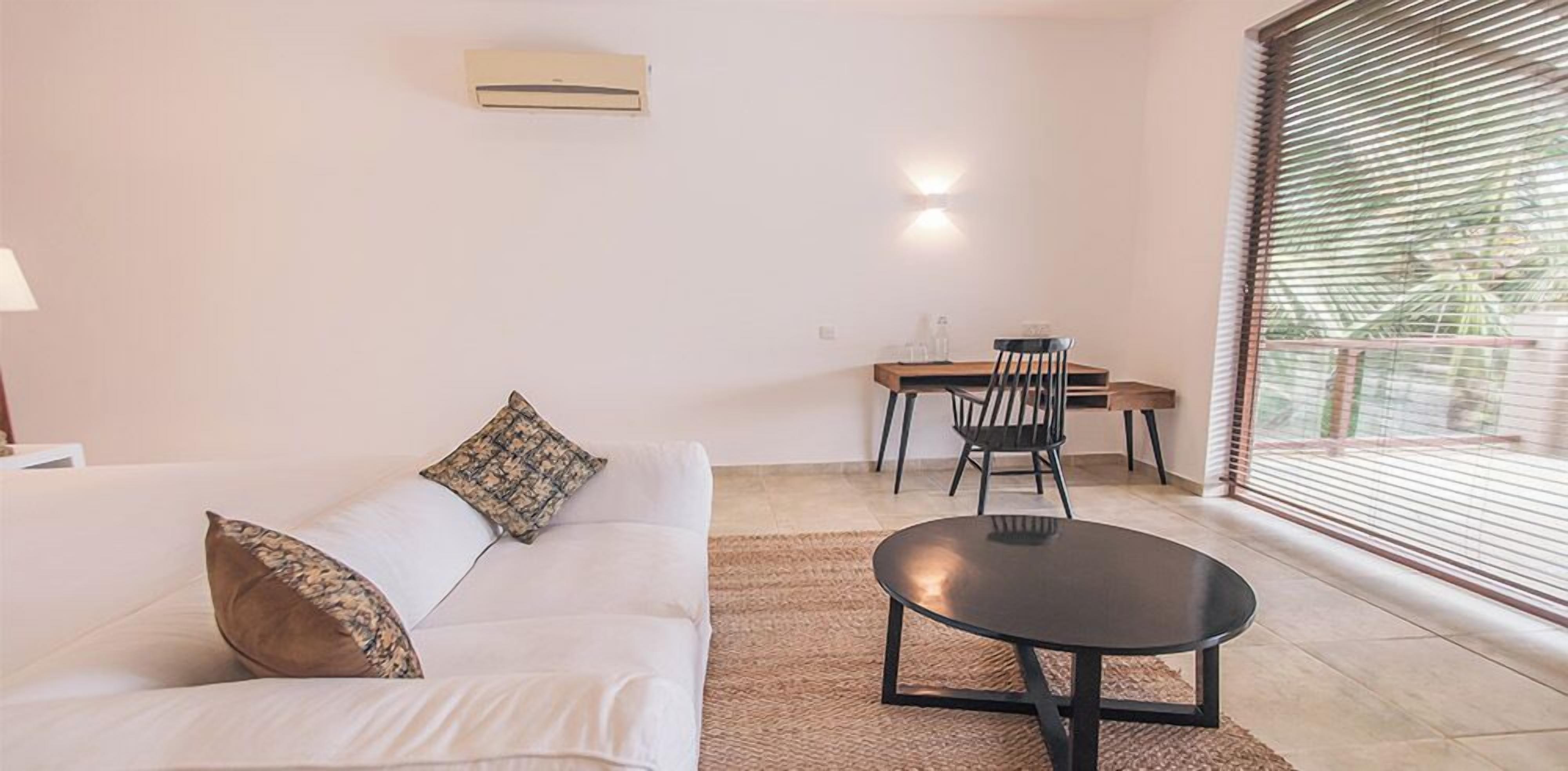 Ein Wohnzimmer mit Sofa, Couchtisch, Esstisch mit Stühlen und einem Fenster mit Jalousien.