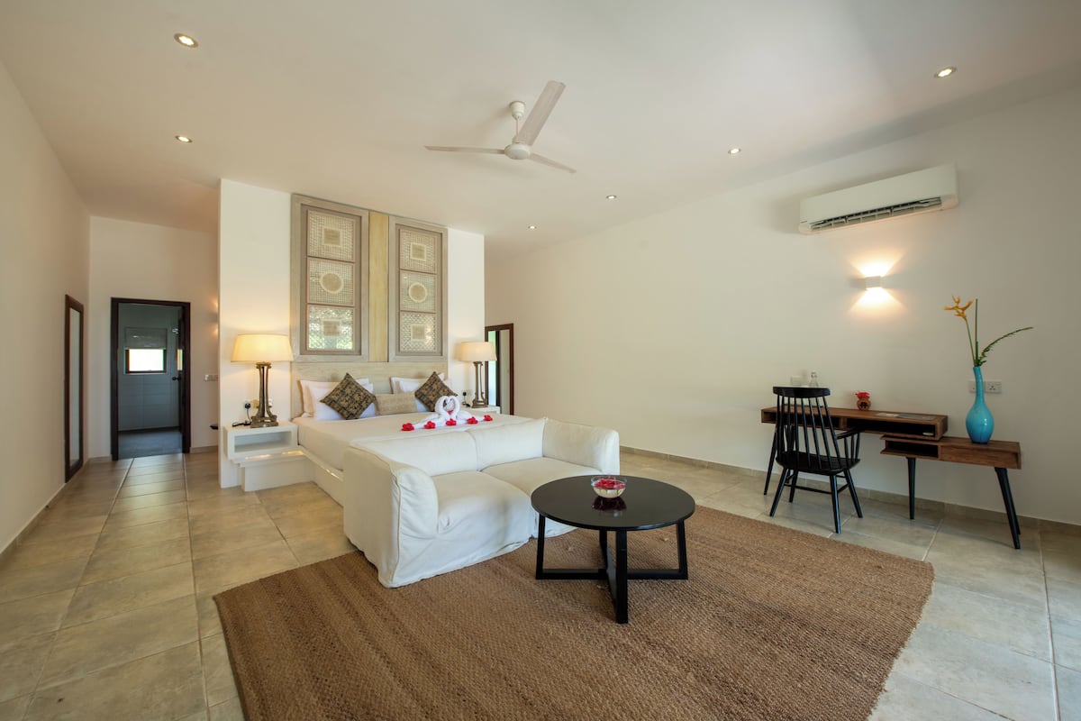 Una habitación de hotel moderna con una cama, un escritorio, una silla, una mesa redonda y un ventilador de techo.
