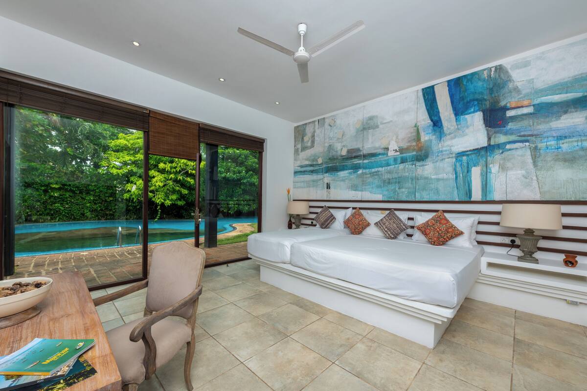 Un dormitorio con una cama grande, una silla, un escritorio con un tazón y vista a una piscina.