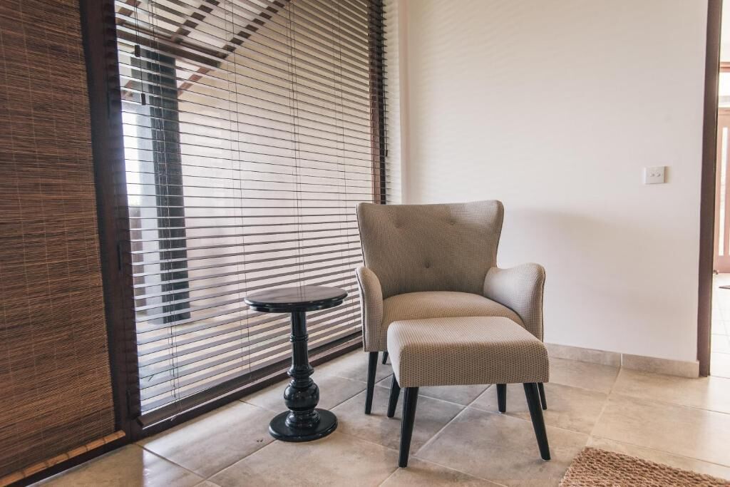 A room with a beige armchair, a small round table, and a window with blinds.