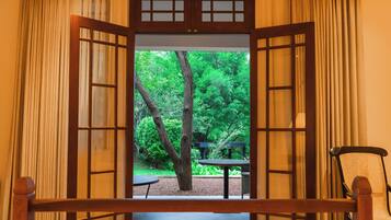 A room with an open wooden door leading to a garden with trees and a table.