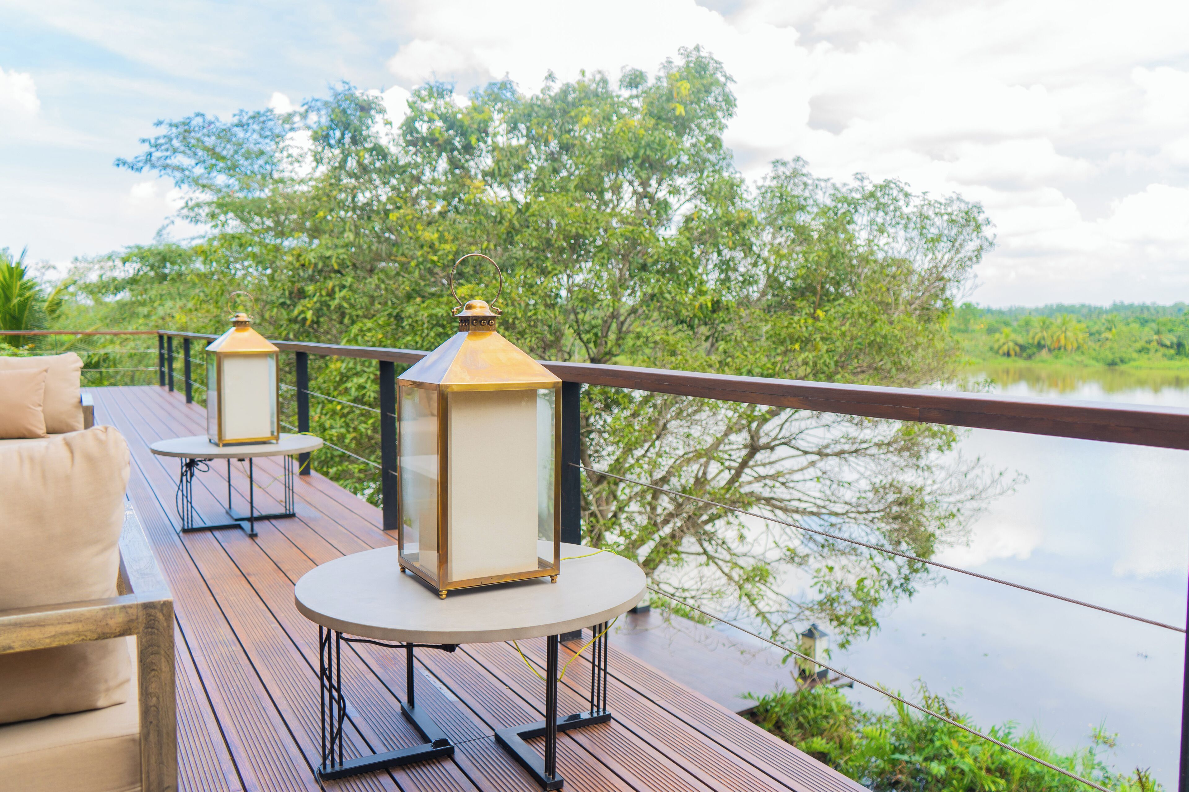 A wooden deck with outdoor furniture and lanterns overlooking a body of water and greenery.