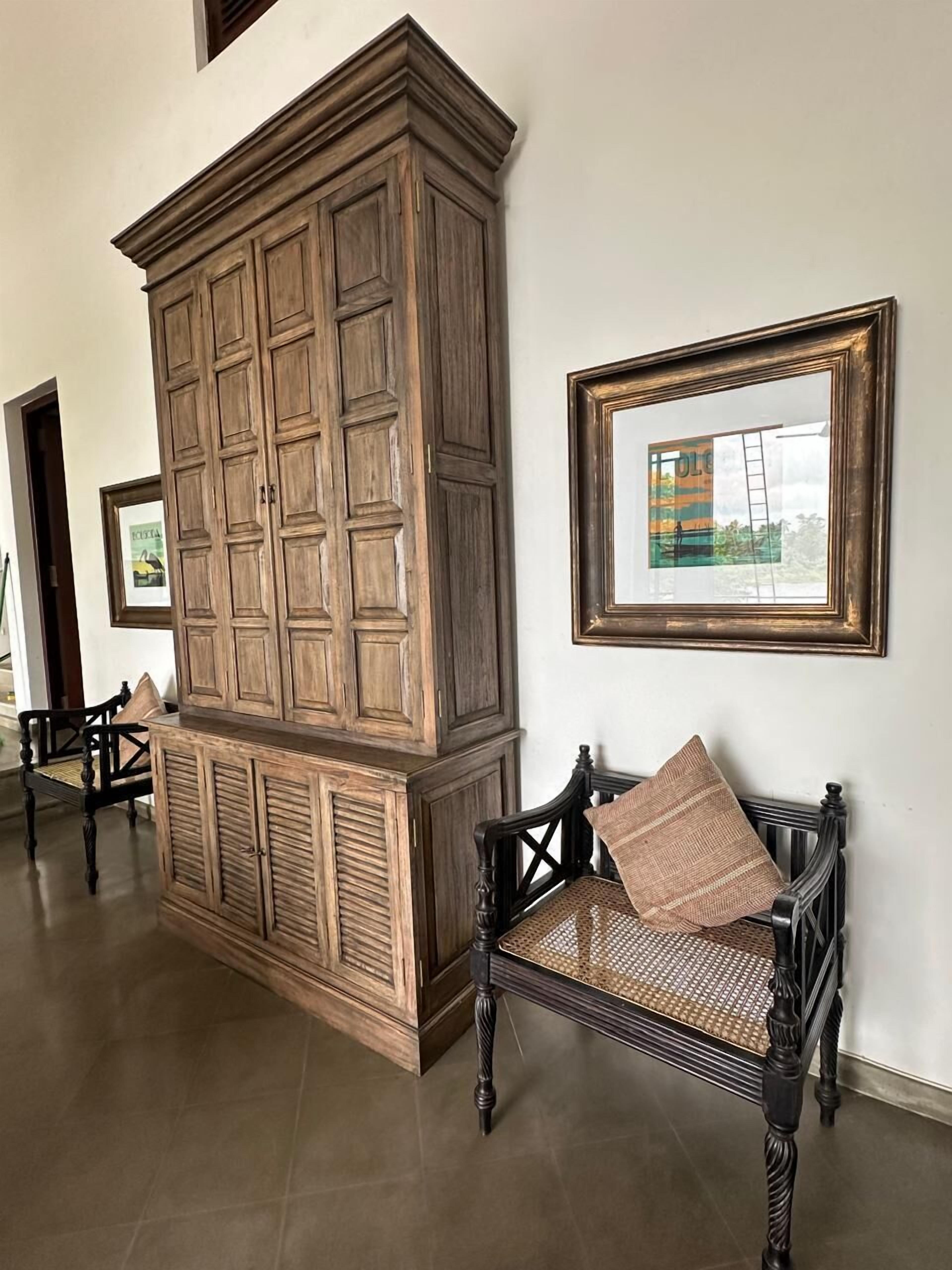 Une pièce comprenant un grand meuble en bois, un banc avec un siège en osier, et des tableaux encadrés accrochés au mur.