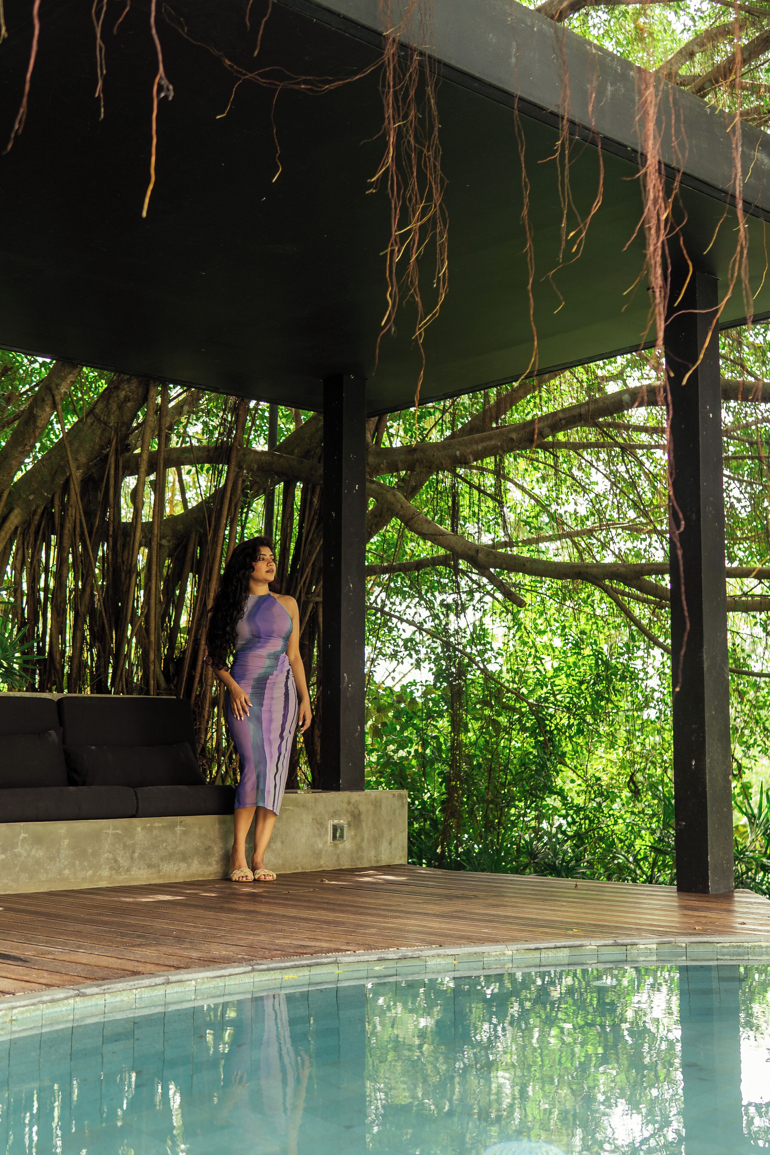 A covered outdoor area with a pool, wooden deck, and a natural backdrop of trees.