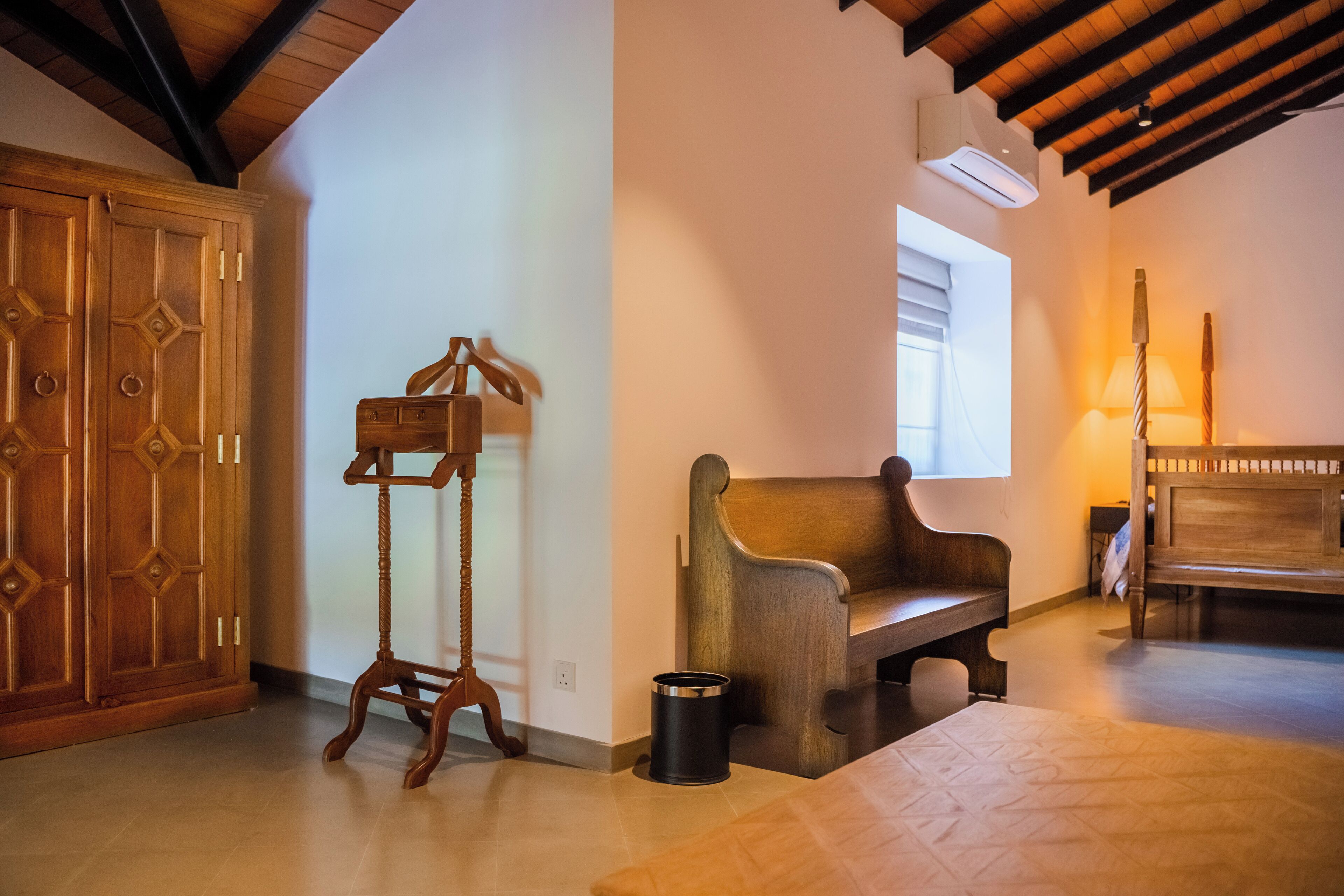Una habitación con un banco de madera, un armario de madera, una mesita y una lámpara.