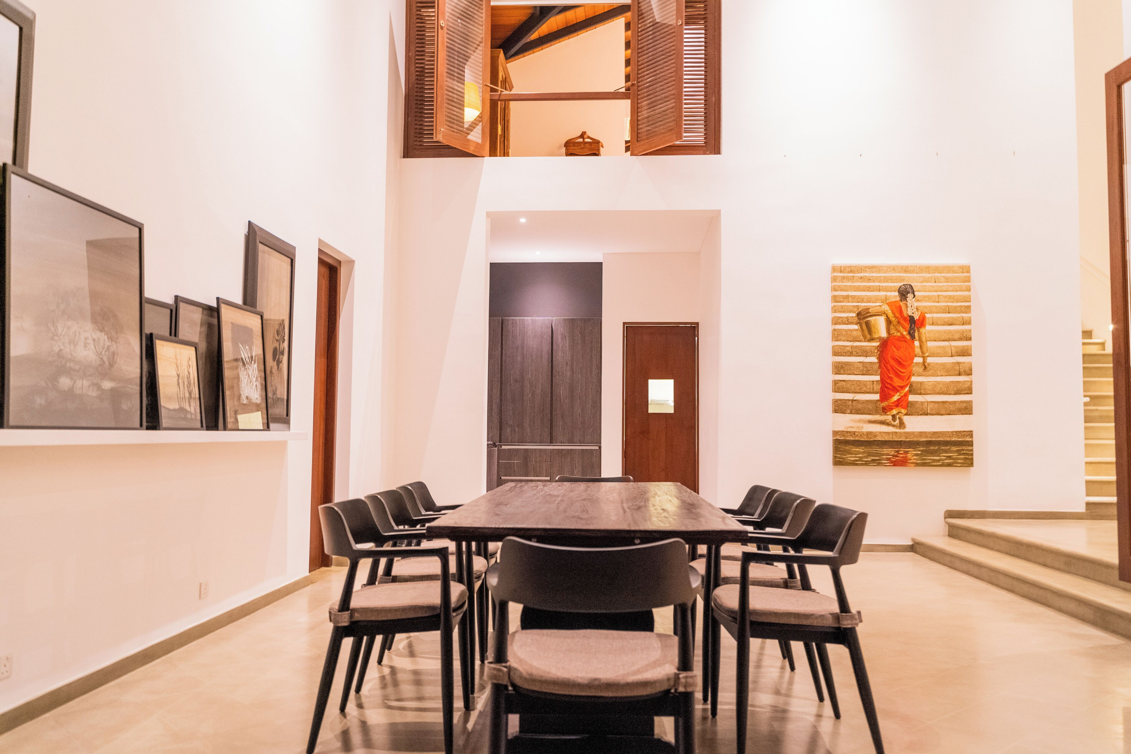 A conference room with a long table and chairs, framed artwork on the walls, and a statue on the staircase.