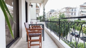 Un balcone con tavolo e sedie in legno, ringhiera in metallo nero e vista su una strada cittadina.