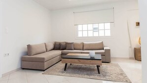 Un soggiorno moderno con un divano modulare beige, un tavolino in vetro e un'ampia finestra con persiane.