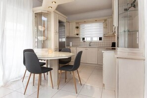 A modern kitchen with white cabinets, a glass dining table, and two chairs. - Faliro Escape Modern Living (Paleo Faliro)