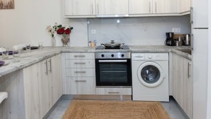 A compact kitchen with a stove, oven, and washing machine, wooden cabinets, and a marble countertop.