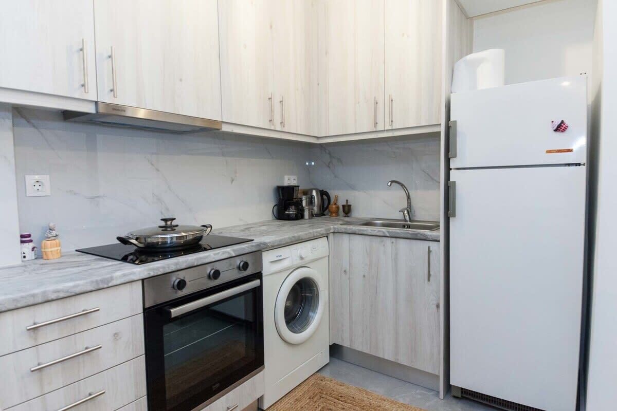Une cuisine compacte avec des meubles blancs, une cuisinière, un four, un lave-linge, un évier et un réfrigérateur.