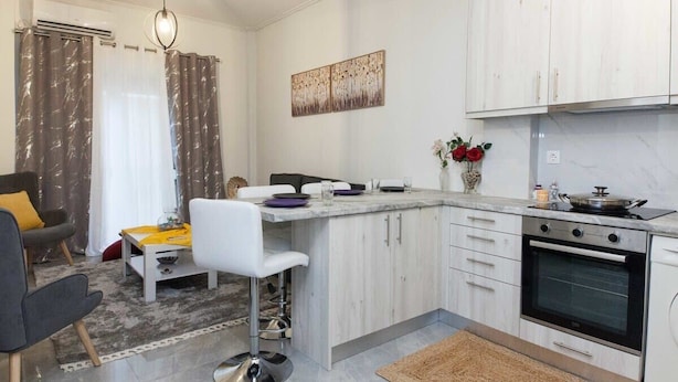 A modern kitchen with white cabinets, a built-in oven, and a dining area with a bar stool and a small table.