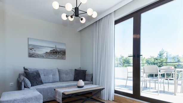 A modern living room with a sofa, ottoman, and coffee table, a painting on the wall, and a balcony with outdoor furniture.