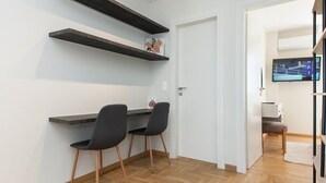 A room with a desk, two chairs, wooden flooring, a white door, and a TV mounted on the wall.