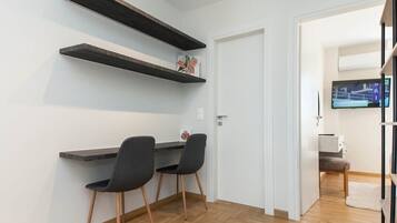 Huoneessa on työpöytä, kaksi tuolia, puulattia, valkoinen ovi ja seinälle asennettu televisio.