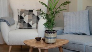 Een ronde houten tafel met een rieten mand waarin een plant, een kleine schaal en een wit bord zitten.