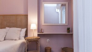 Een slaapkamer met een bed, een bedlamp, een spiegel, een plank met een plant en rieten manden.